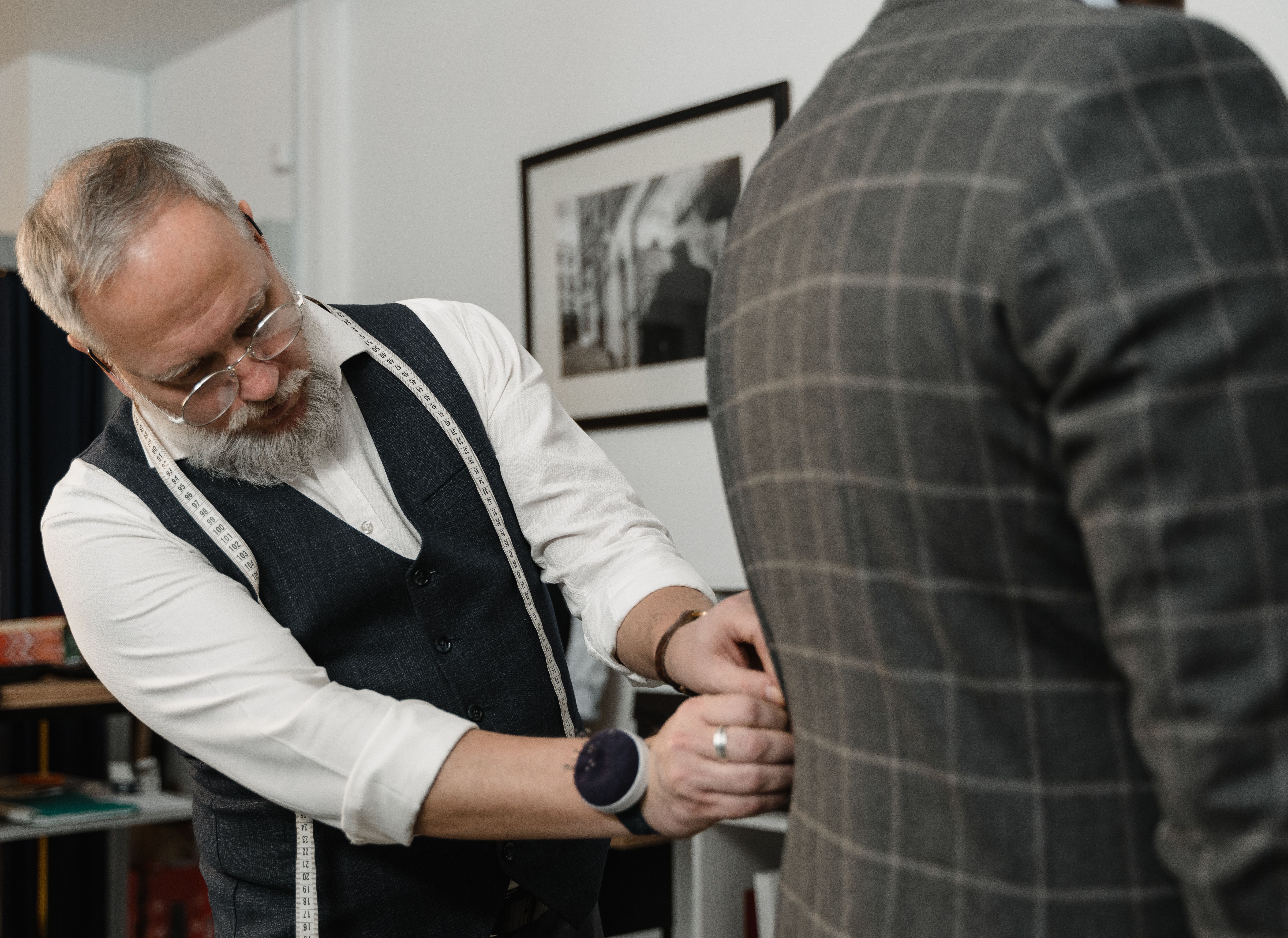 Tailor carefully fitting a suit jacket to a client in a bespoke atelier.