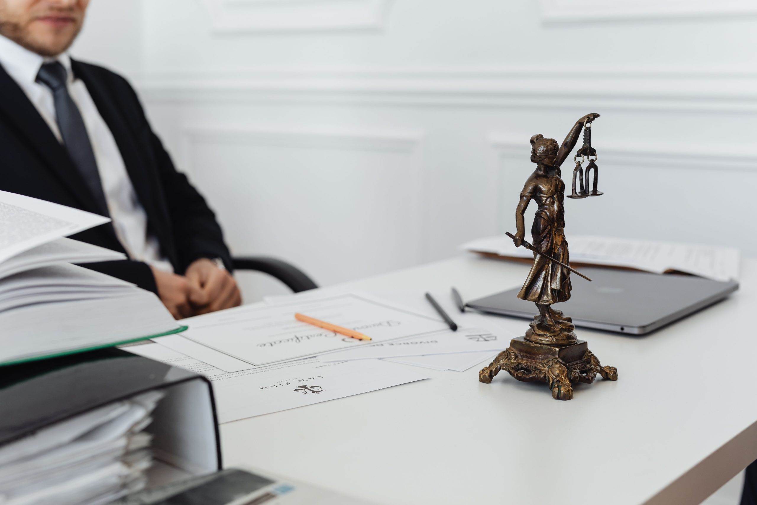 Legal professional's desk with Lady Justice statue, legal documents and a laptop, illustrating law firm work on large civil cases
